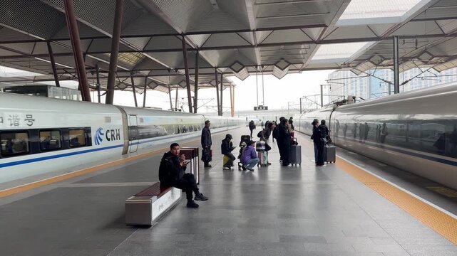 Passengers waiting on a modern Chinese high-speed rail platform as CRH bullet trains arrive and depart on both sides. Travelers with luggage stand between two sleek white trains with blue stripe liver