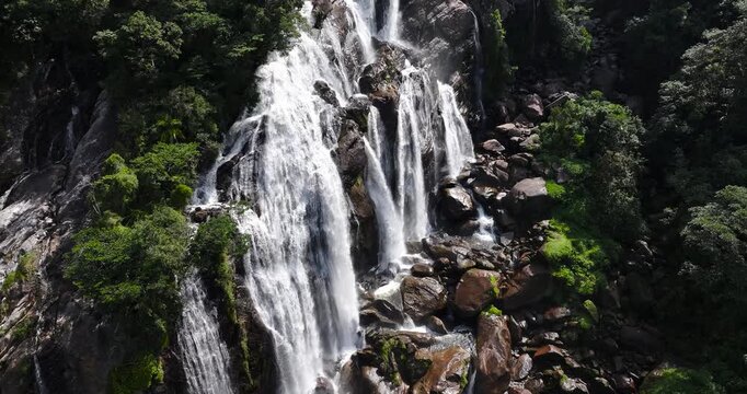 Cinematic aerial 4K footage of Veu da Noiva waterfall located in the Serra do Mar, Brazil. The scene showcases powerful cascading water flowing over rocky cliffs surrounded by dense tropical rainfores