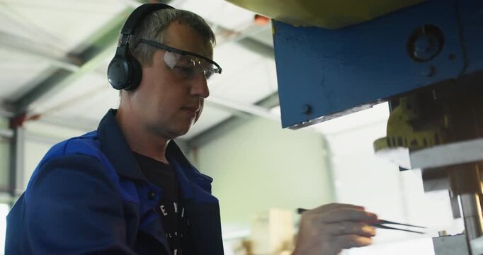 Punch press operator working at metal stamping machine, controlling sheet position during industrial production
