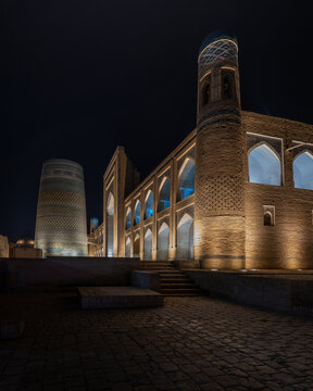 View of the illuminated Kalta Minor Minaret and Mohammed Amin Khan Madrasah at night with intricate tilework and stone arches Khiva, Xorazm Region, Uzbekistan.