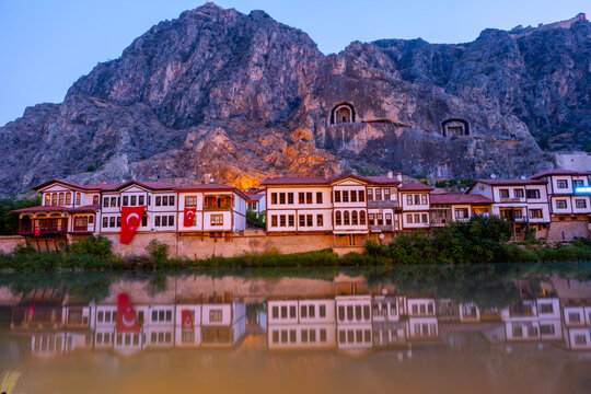 Cinematic photograph of Amasya at twilight. Historic Ottoman houses and illuminated Pontic King Rock Tombs reflecting on the calm Yesilirmak River in Turkey. Beautiful evening scenery and heritage.