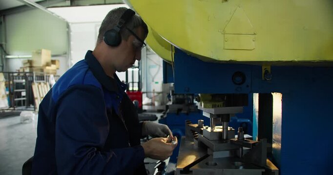 Machine operator working at metal stamping press in factory environment. Industrial workforce and production line concept