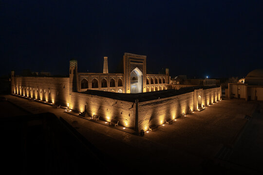 View of the illuminated historic madrasah and ancient stone walls at night in Khiva, Xorazm Region, Uzbekistan.