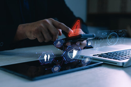 User using smartphone with cybersecurity warning, shield and lock icons beside laptop, concept of mobile data protection and online threat detection.