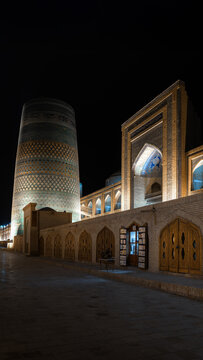 View of the illuminated Kalta Minor Minaret and Mohammed Amin Khan Madrasah at night with traditional wooden doors in Khiva, Xorazm Region, Uzbekistan.