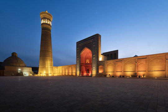 View of the illuminated Po-i-Kalyan complex featuring the Kalyan Minaret and mosque entrance at dusk in Bukhara, Bukhara Region, Uzbekistan.