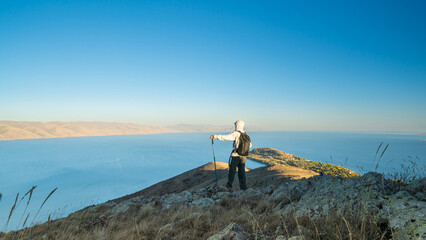 Obraz premium Traveler standing on a rocky hill overlooking Lake Sevan, Armenia. Stunning panoramic landscape of mountains, lake, and clear blue sky.