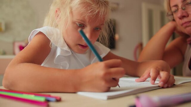 Schoolgirl writing in exercise book, mother sitting next to her assisting with homework. Family support in education