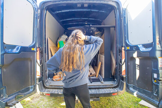 Rear view of a young woman looking at wooden furniture and belongings in a delivery van while moving to a new home.