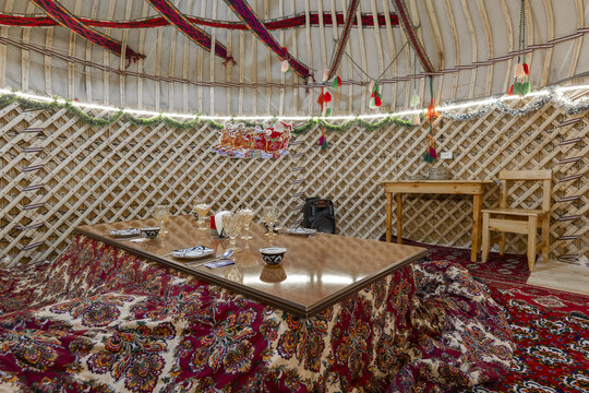 View of the interior of a traditional yurt featuring a low table covered with a patterned carpet and wooden lattice walls in Bukhara, Bukhara Region, Uzbekistan.