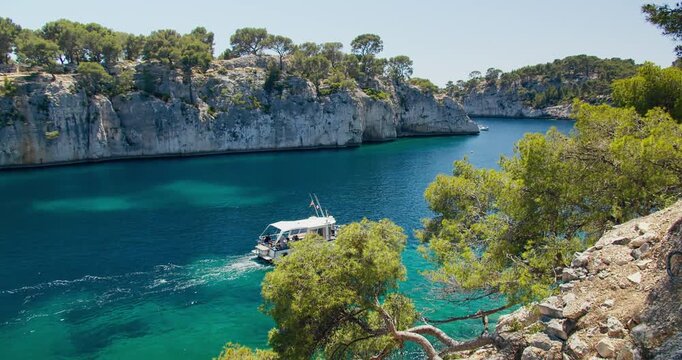 Tourist boat entering a natural limestone inlet on French Riviera near Cassis. Calm water, marina area and rocky coastal landscape