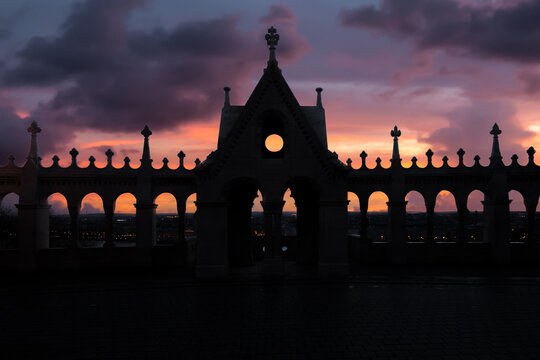 View of the silhouetted arches and spires of Fisherman's Bastion against a dramatic sunset sky in Budapest, Hungary.