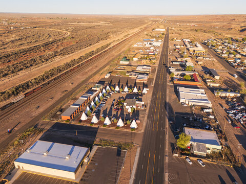 Holbrook, United States - 05 April 2026: Aerial view of the iconic Wigwam Motel with its teepee-shaped rooms along Route 66, featuring a passing train on the nearby railway and the desert landscape.