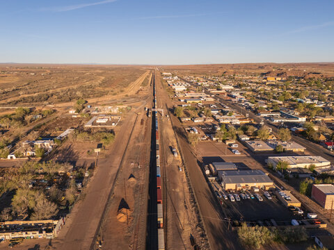 Holbrook, United States - 05 April 2026: Aerial view of a long freight train traveling on tracks through the desert town of Holbrook, surrounded by arid landscape and low-rise buildings.
