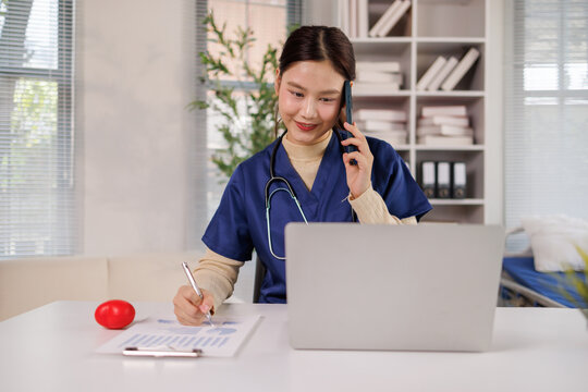 Asian nurse multitasking with smartphone, laptop, and patient charts