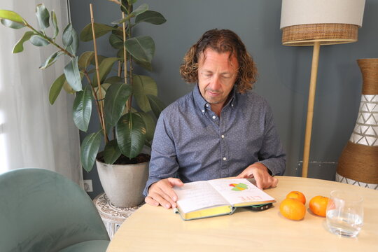 Man with a blue shirt, reading a Journal at Table and a grey wall behind
