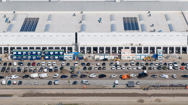 Lelystad, Netherlands - 21 April 2026: Aerial view of the JYSK DCL construction site featuring a large warehouse with loading docks, solar panels, and a busy parking area.