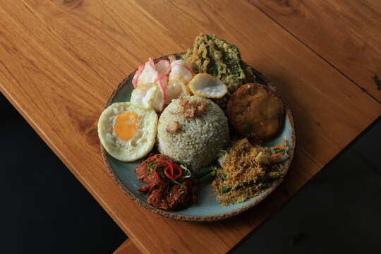 Nasi Campur Bali, a typical dish from the Bali region of Indonesia, consists of rice and side dishes such as spicy chicken, saut&eacute;ed vegetables, fried egg, fried food, and crackers. Served on one plate