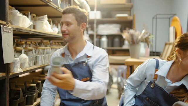 Male and female small business caucasian owners wearing blue aprons pricing handmade ceramic pottery using a label gun and scanning barcodes inside a retail craft shop. Teamwork and inventory tracking