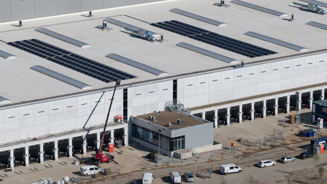 Lelystad, Netherlands - 21 April 2026: Aerial view of the JYSK DCL construction site featuring a large white warehouse with loading bays, solar panels on the roof, and a crane with workers.