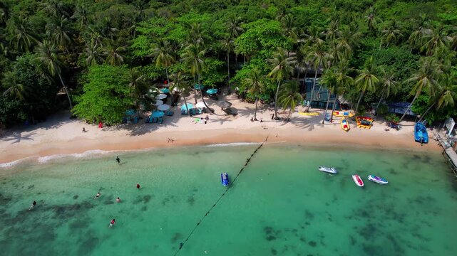 Stunning aerial footage of Hon Vong Island Beach with turquoise blue water and sandy beach with tourist boats anchored and people swimming on a hot summer day in Phu Quoc South Vietnam