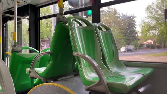Bus Seats: Modern bus interior with empty green seats near window with natural daylight and trees in background.