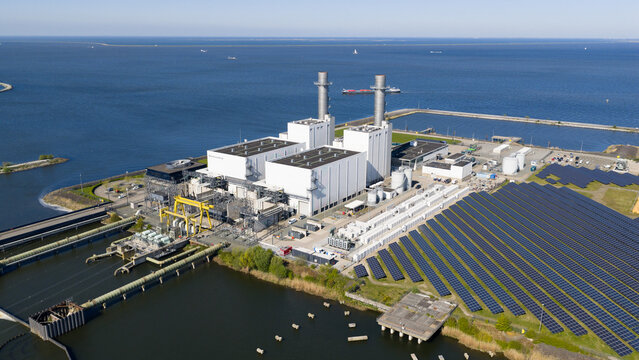 Lelystad, Netherlands - 21 April 2026: Aerial view of the Maxima plant power station and offshore wind turbines along the coast under a clear blue sky.