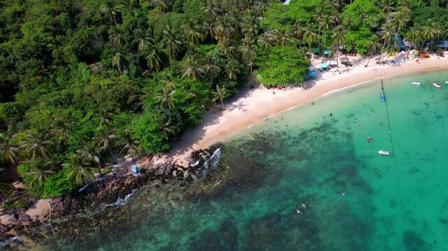 Stunning aerial footage of Hon Vong Island Beach with turquoise blue water and sandy beach with tourist boats anchored and people swimming on a hot summer day in Phu Quoc South Vietnam