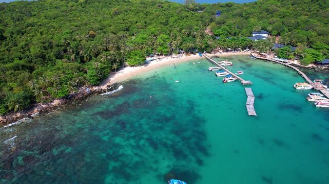 Stunning aerial footage of Hon Vong Island Beach with turquoise blue water and sandy beach with tourist boats anchored and people swimming on a hot summer day in Phu Quoc South Vietnam