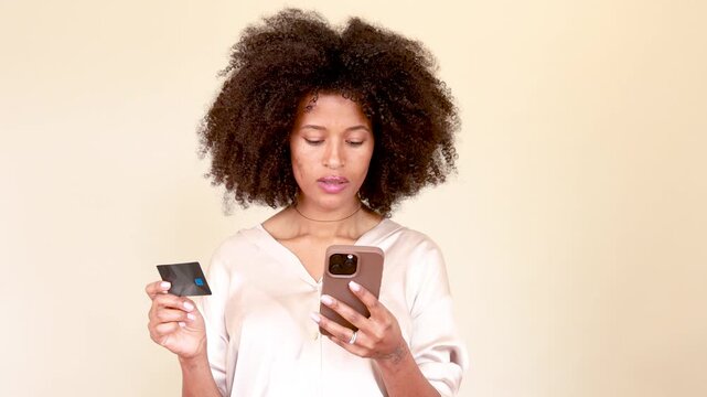 Afro-haired woman shopping online, entering credit card details on her smartphone, showing various emotions
