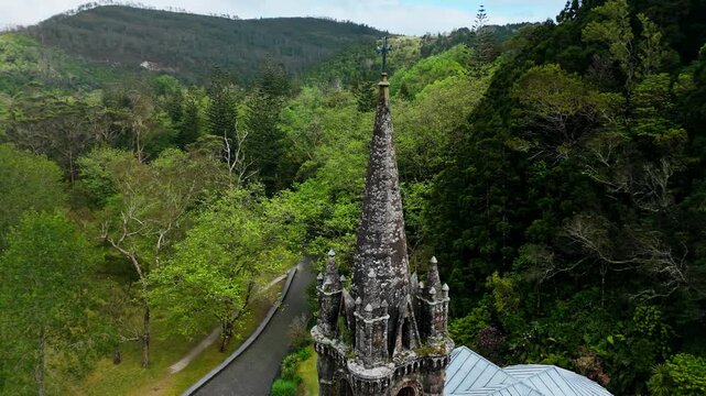 Close aerial view of gothic tower of Capela de Nossa Senhora das Vitorias framed by surrounding forest hills on Sao Miguel, Azores