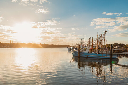 Fishing boats docked at harbour during golden hour with sun reflecting on water