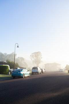Urban street scene with morning light through mist hiding houses along road