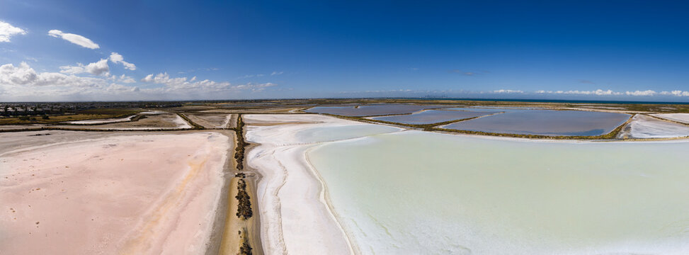 Aerial panorama view of colourful coastal salt ponds under blue sky
