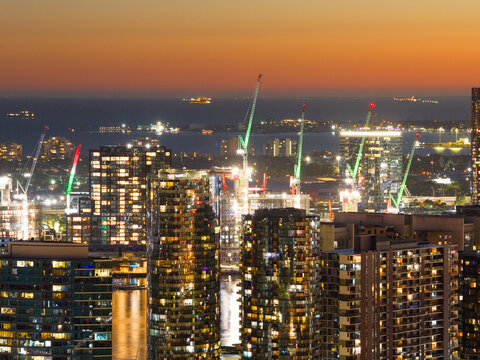 Aerial view of city light and cranes on top of highrise buildings with a ships in the distance
