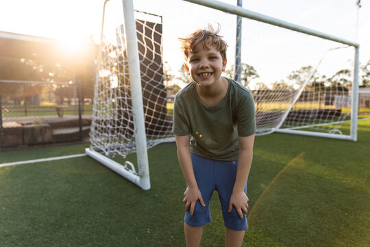 blonde boy leaning forward with hands on his knees in front of a soccer goal