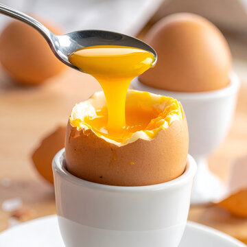 Soft boiled egg in egg cup with runny yolk and spoon about to drip deliciousness