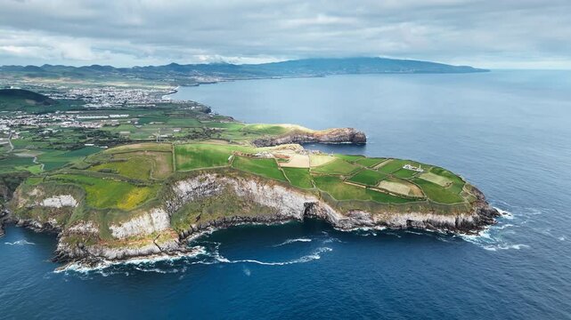 Green agricultural cliffs above Atlantic Ocean with patchwork fields and rugged coastline in Azores. Aerial view