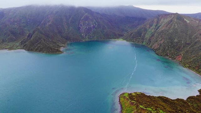 Natural caldera lake surrounded by volcanic mountains and forested slopes, low clouds moving across the landscape. Lagoa do Fogo, Sao Miguel island, Azores, drone view