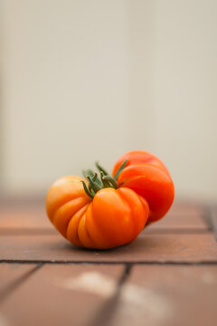 A ripe heirloom tomato with green stems sit on a rustic wooden surface