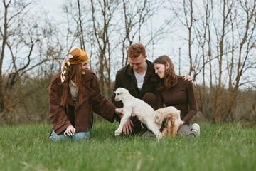 Fototapeta premium Family, outdoor, dogs, friends enjoying a sunny park scene, a candid moment of bonding and affection, warm clothing and green grass, natural light, casual lifestyle in a rural setting