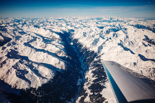 Breathtaking aerial view of the snow-covered Alps mountain range captured from an airplane window during a winter flight