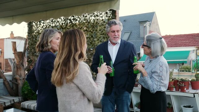 Four mature friends talking and toasting with beer bottles during a social gathering on a terrace