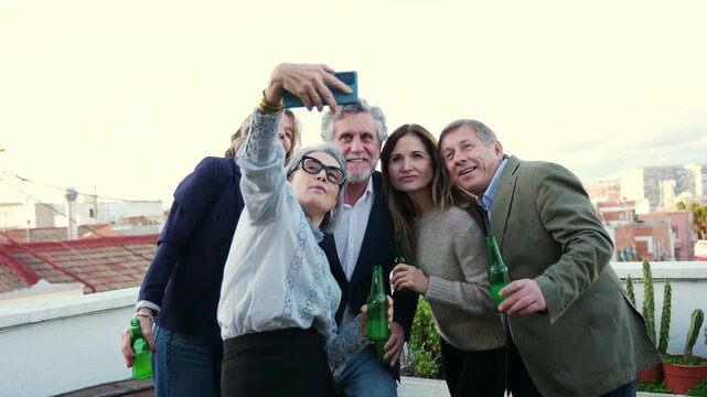 Cheerful group of senior friends drinking beer and taking a selfie with a smartphone on a terrace