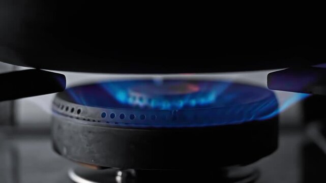 Macro close up of domestic kitchen gas stove burner igniting bright blue flames under a black pan, natural gas energy cooking equipment
