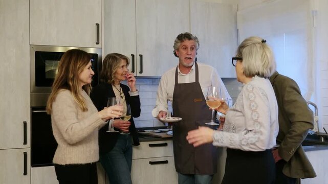 Group of elegant mature friends socializing over wine and appetizers in a modern home kitchen
