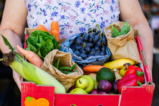 Box of fresh organic fruit and veggies from local Box Divvy hub held by woman