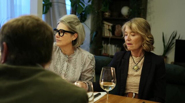 Mature friends talking, eating, and laughing while enjoying a meal together at a dining table
