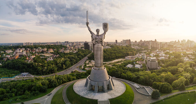 Kyiv, Ukraine - 27 May 2019: Aerial view of the Motherland Monument statue with its sword and shield overlooking the lush green hills and city skyline during sunset.