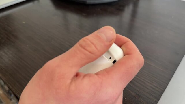 A person opens and closes a small plastic earbud case using one hand